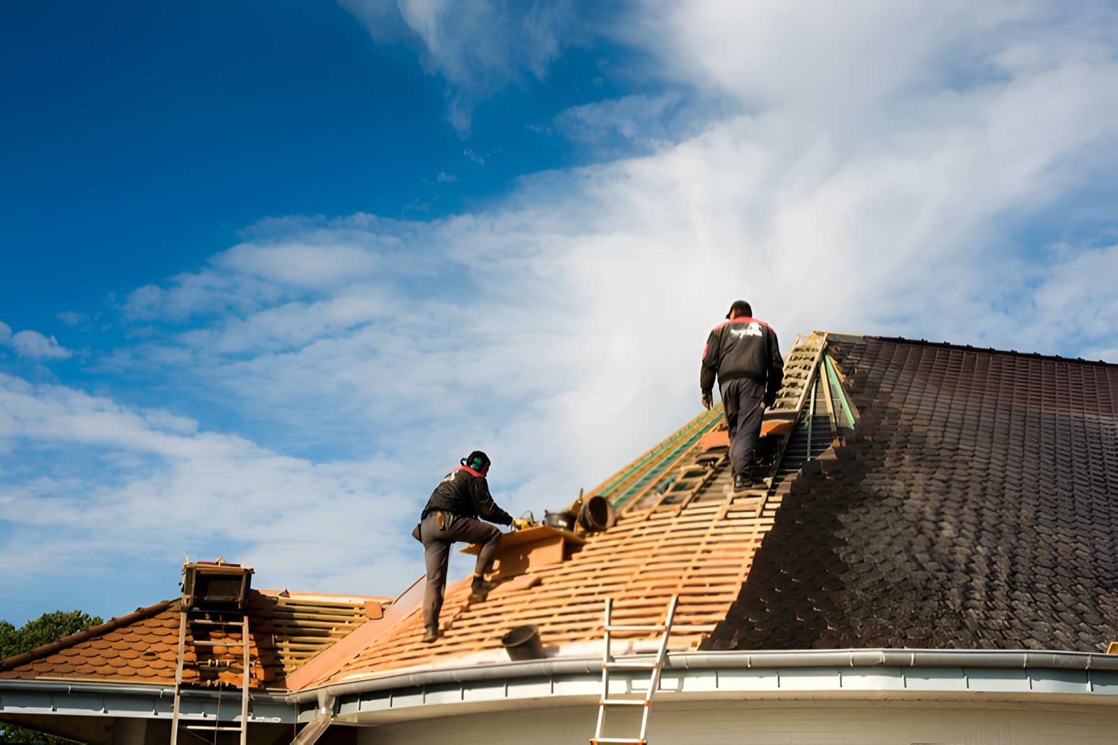 Dachdecker bei der Arbeit auf dem First eines großen Daches vor blauem Himmel